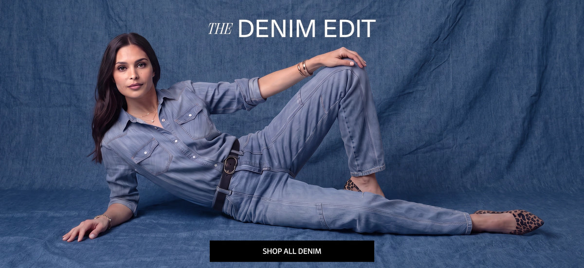 A woman reclining on a blue fabric backdrop wearing a light blue denim shirt and matching denim jeans, with leopard-print shoes. The text 'THE DENIM EDIT' appears at the top, and a black CTA at the bottom reads 'SHOP ALL DENIM'.