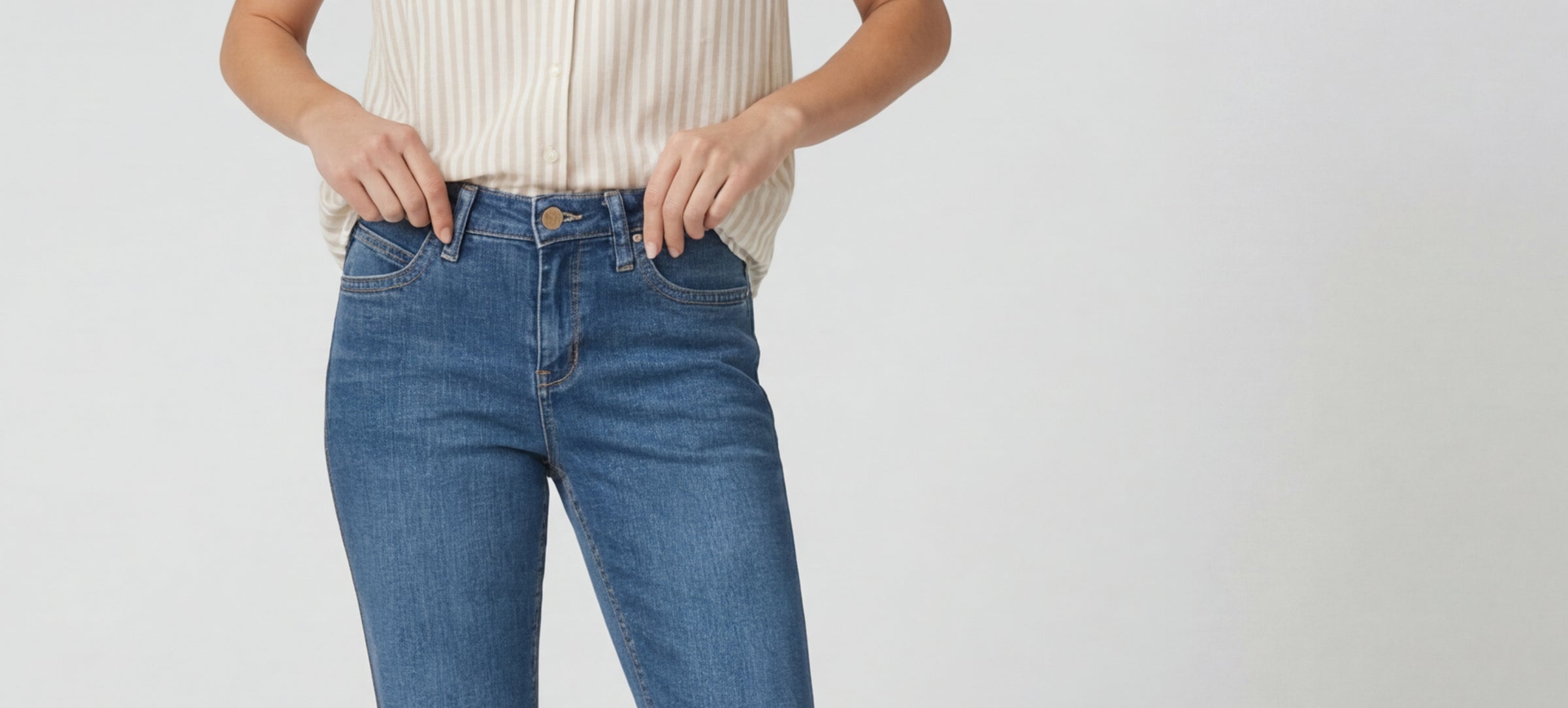 Person wearing blue jeans and a beige top on a plain background